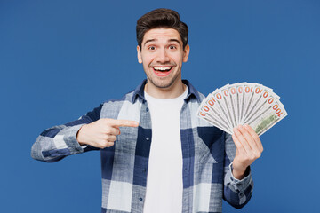 Wall Mural - Young surprised man he wear shirt white t-shirt casual clothes hold in hand point index finger on fan of cash money in dollar banknotes isolated on plain blue cyan background studio Lifestyle concept