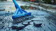 close-up of a blue broom being used to clean the grey, crumbling concrete sidewalk outside