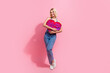 Full length photo of adorable nice girl dressed colorful tank denim pants embrace big paper heart isolated on pink color background