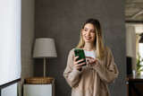 Fototapeta  - Young woman wearing sweater using smartphone at home, communication and social network concept,