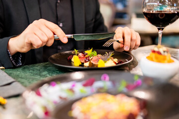 Sticker - Person in black attire about to enjoy a colorful gourmet meal in an elegant setting, with a glass of red wine and additional dishes blurred in the foreground