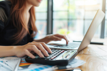 Aufkleber - A woman is using a calculator on a table with a laptop and some papers. She is focused on her work and she is in a serious mood