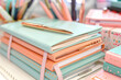 © Wei Ze - Stacked pastel notebooks with a golden pen on top, amidst a blur of colorful stationery items