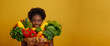 A woman is holding a bunch of vegetables, including broccoli and peppers. She is smiling and happy. portrait happy african american woman holding fresh fruits and veggies in isoalated background
