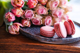 Fototapeta Tulipany - Beautiful pink roses and tulips with sweet delicacies. Sweet macaron pastries on a wooden table. Still life background for mother's day and weddings. Close-up.
