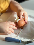 Fototapeta Desenie - Baby hands shelling boiled egg. Breakfast time. Closeup view