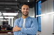 © Tetiana - Portrait of a young hispanic male programmer and developer standing in the office, crossing his arms over his chest and looking at the camera with a smile.