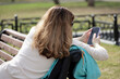 Woman with long hair sitting with smartphone on а street bench in spring