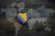 wooden heart with national flag of bosnia and herzegovina near world map on the wooden background.