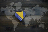 Fototapeta  - wooden heart with national flag of bosnia and herzegovina near world map on the wooden background.