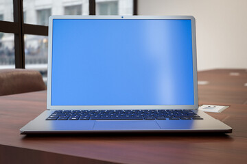 Poster - Laptop mockup with blue screen on wooden office table. Cropped shot of modern workspace with blank blue screen laptop