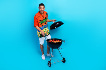 Canvas Print - Full length photo of cheerful positive guy dressed print shirt enjoying grilling sausages isolated blue color background