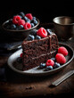 Close-up slice of delicious chocolate cake with summer berries in a dark plate on wooden table.