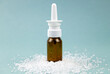 Homemade saline nasal spray bottle on pile of sea salt grains on blue background, studio shot. Lot of copy space.