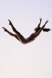 Fototapeta Nowy Jork - In-flight gymnast: A female acrobatics performer leaps mid-air in a graceful routine
