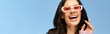 A pretty woman wearing pink sunglasses in a studio on a blue background, making a comical expression.