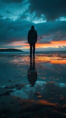 Wall Mural - Silhouette of a person standing on the beach at sunset with reflection