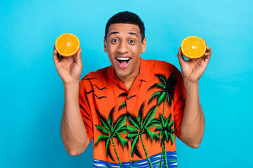 Poster - Photo of excited funky guy dressed print shirt holding two orange halves isolated blue color background