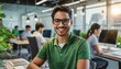 © Marko - Cheerful man with glasses and a green t-shirt is smiling at the camera, seated in a modern office with co-workers and computers in the background