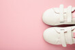 Stylish white children's sneakers on pink background, top view