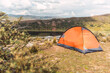 orange tent on top of a mountain with a lake in the background and blue sky and clouds in the middle of the forest in the Andes mountain range
