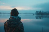 Fototapeta Do akwarium - A serene portrait captures a moment of deep contemplation, with an individual gazing over a peaceful, mist-covered lake as dawn breaks.