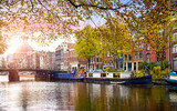 Fototapeta  - Amsterdam, Netherlands. Panoramic view of autumn Dutch city. Famous channel Amstel river. Evening cityscape. Colorful sunset scene famous travel destination in Europe. Romantic traveling place