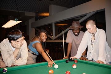 Diverse group of young friends playing pool together in nightclub with camera flash