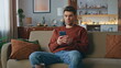 Frowning man looking mobile phone screen on cozy couch. Serious guy messaging