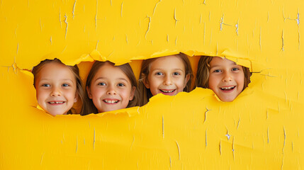 Wall Mural - Cheerful children peering out from behind a yellow solid background with copy space