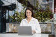 © Anton Pentegov - young focused freelancer working with notebook in cafe, typing text and smiling, concentrated caucasian businesswoman in white shirt, green plants in background, freelance concept