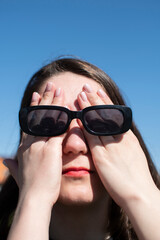 Wall Mural - Conceptual portrait of a woman in sunglasses. Young attractive woman covering her face with a her hands	