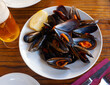 Delicious baked mussels in shells served on plate with slice of lemon and beer. Popular seafood appetizer..