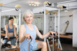 Sporty elderly woman practicing pilates stretching exercises on combo chair. Healthy lifestyle and fitness concept..