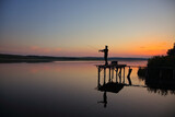 Fototapeta Do akwarium - Amazing sunset over calm lake with fisherman catching fish.