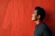 Portrait of a young Asian man standing against a red wall.