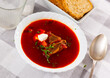 Healthy Russian beetroot soup with vegetables and meat decorated by sour cream and parsley served on table in restaurant