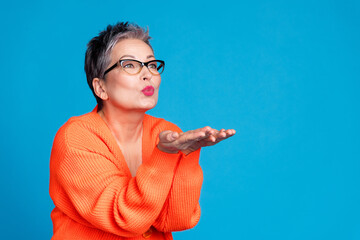 Sticker - Portrait of aged lady hands send air kiss empty space wear orange cardigan isolated on blue color background