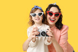 Fototapeta Panele - Beautiful pin-up woman and her daughter with photo camera on yellow background