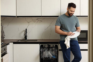 Sticker - Smiling man wiping plate near open dishwasher in kitchen