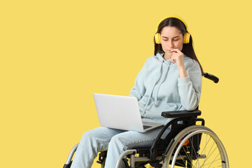 Thoughtful young woman in wheelchair with headphones and laptop on yellow background