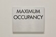 Maximum Occupancy sign on white interior wall in commercial building, copy space. NFPA Fire Marshal requirement.