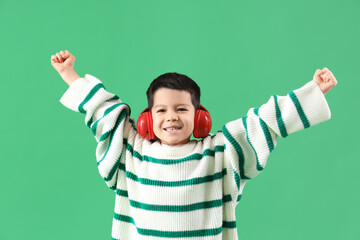 Wall Mural - Cute little Asian boy in adult clothes with headphones on green background