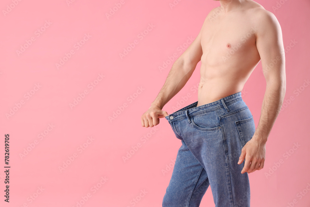 Handsome young sporty man in loose jeans on pink background. Weight loss concept