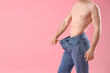 Handsome young sporty man in loose jeans on pink background. Weight loss concept