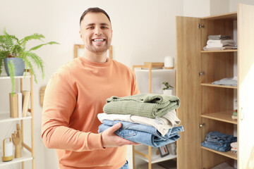 Young man with stack of clothes near closet at home