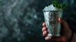 Hand holding chilled metal cup with crushed ice and mint leaves against blue textured background