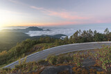 Fototapeta Las - Long curvy forest asphalt road over the hills. Beautiful curved road in the forest. Side view of road with fog at sunrise.