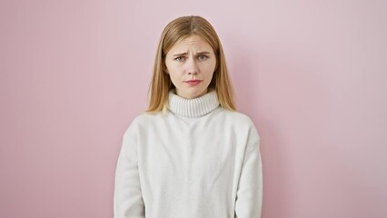 Wall Mural - Disgruntled, beautiful blonde girl with a skeptic frown and nervous gaze stands isolated, grappling with an upset face over a problem. pink background augments the negative aura.