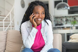 Fototapeta  - Laughing african american woman with dreadlocks talking at phone indoors at living room